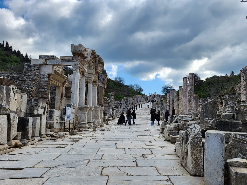 Curetes Street and the Temple of Hadrian. This view shows the beginning of Curetes Street, the main thoroughfare of Ephesus stretching from the Gate of Hercules to the Library of Celsus. The ornate arched structure visible in the foreground on the left is the Temple of Hadrian. Dedicated to the 2nd-century Roman Emperor Hadrian, the temple is considered one of the most beautiful buildings in Ephesus, featuring exquisite reliefs of Tyche (the goddess of fortune) in the center of the front arch and Medusa in the inner arch.