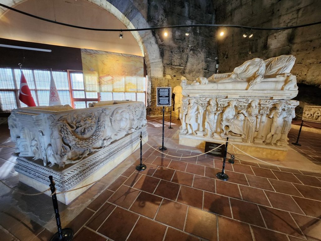 Internal exhibition hall displaying large sarcophagi adorned with reliefs of Greek mythology and ancient funerary art