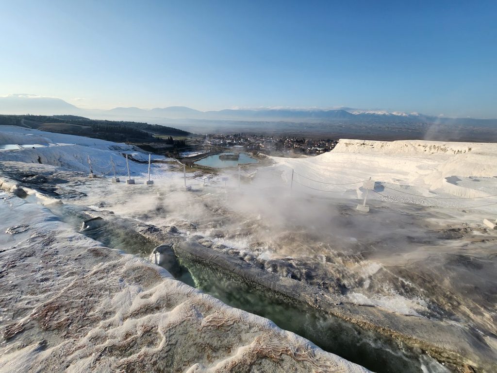 A small stone channel slicing through the white travertine walls where crystal-clear thermal water rushes down