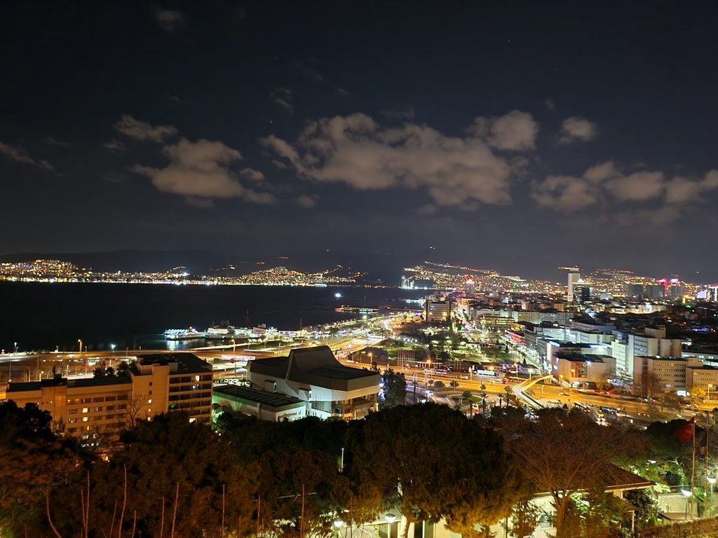 The breathtaking night skyline of Izmir, with dazzling city lights reflecting softly off the calm Aegean Sea.
