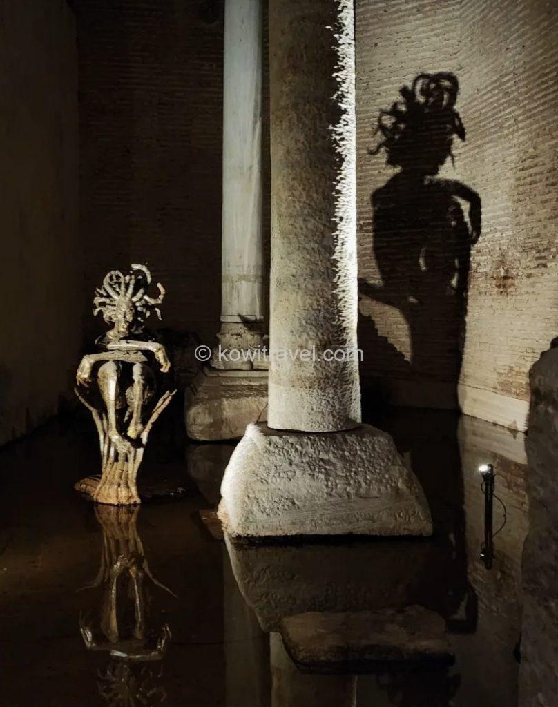 The dramatic lighting casts a massive, eerie shadow of Medusa—with her snake-like hair—onto the rear wall.